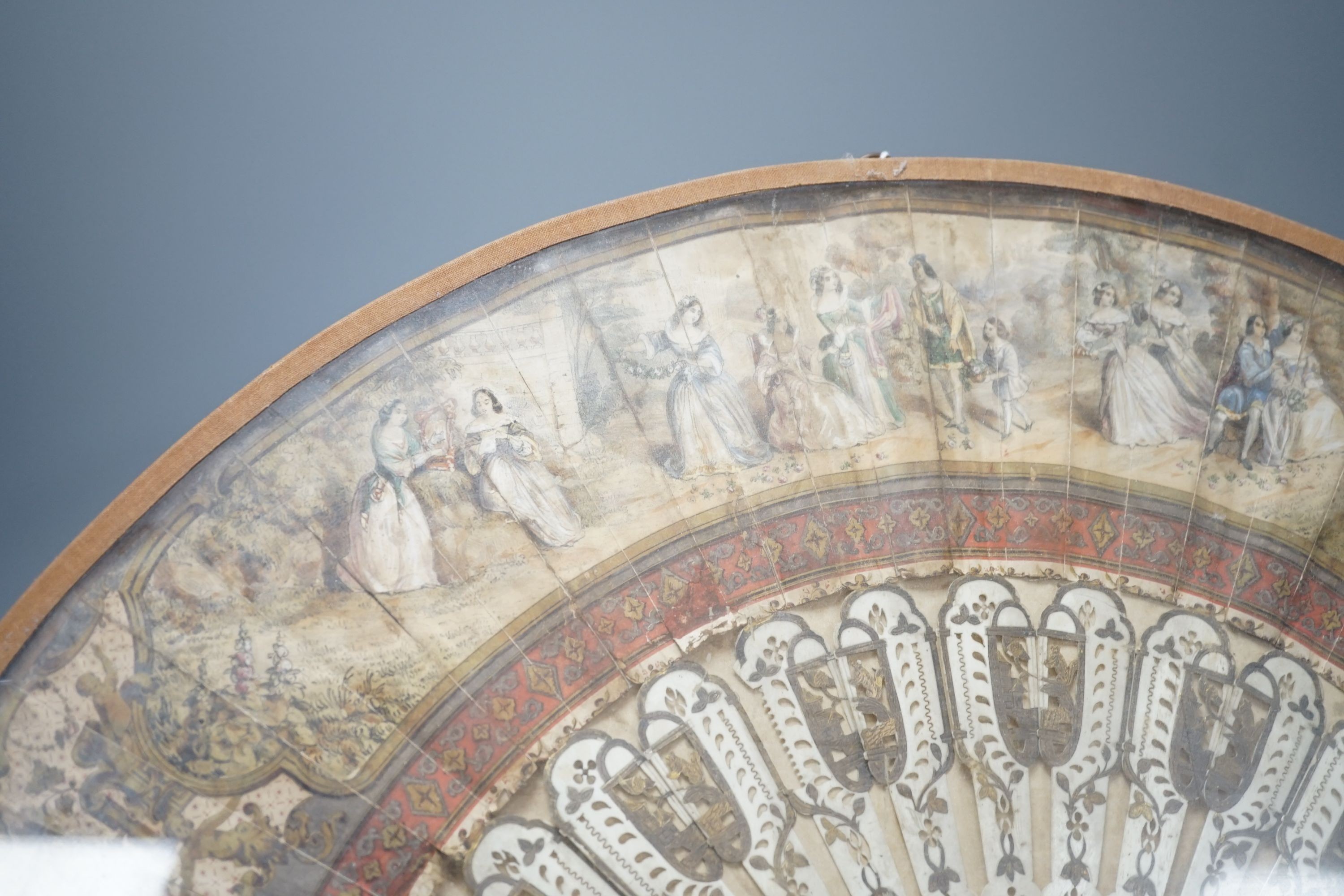 A cased 19th century French lithograph paper leaf and bone stick fan, 56 cms wide.